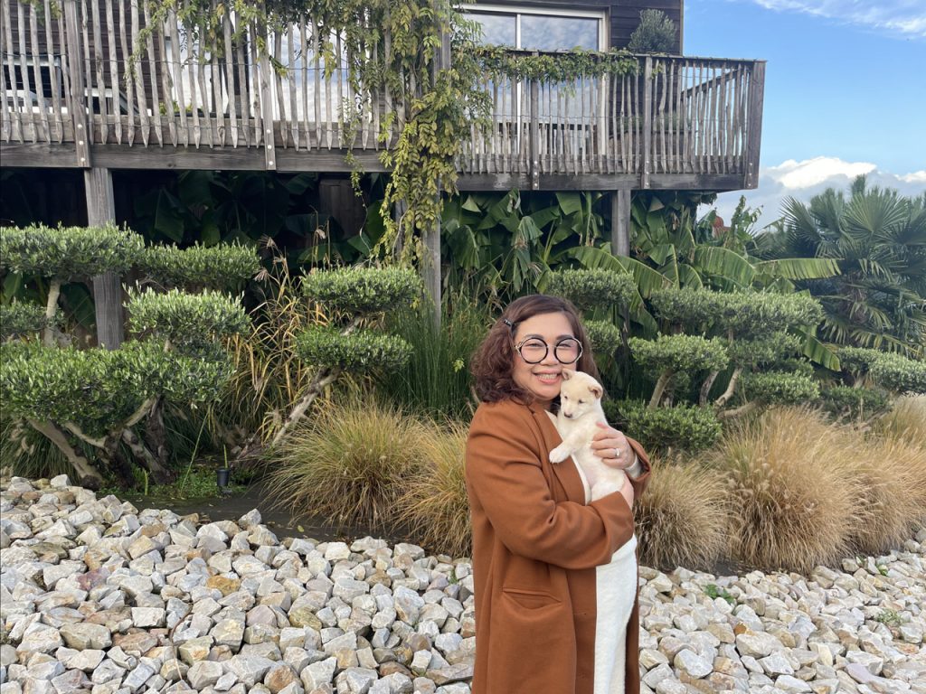 Chiot mame shiba crème dans les bras de sa maîtresse, devant une maison sur pilotis